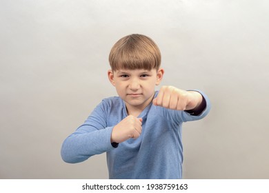The boy in anger stretched out his fist for a blow on a gray background.