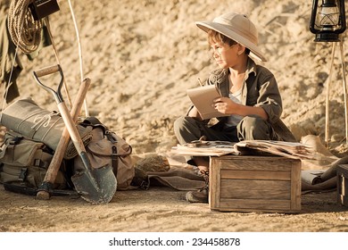 Boy archaeologist after excavations take notes in a notebook in a summer tent on a hot afternoon