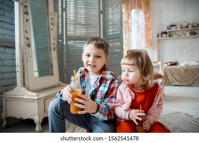 Boy and baby girl drink natural juice at home,bright living room. Natural orange juice in a glass. healthy products, joyful children. The girl puffed out her cheeks. tasteless juice. healthy juice