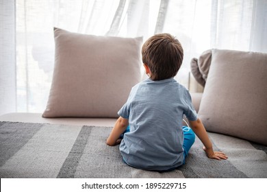Boy from back, looking trough the window. Little boy sitting on sofa at home. Child autism. Depressed little boy sitting on the sofa. Unhappy child  Alone at home. Upset.