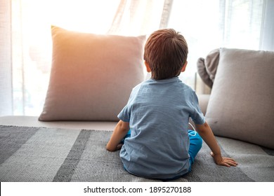 Boy from back, looking trough the window. Little boy sitting on sofa at home. Child autism. Depressed little boy sitting on the sofa. Unhappy child  Alone at home. Upset.
