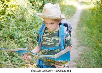 boy with a backpack in hat looking on the map. travelling background. camping with  children. summer time activity.                  
