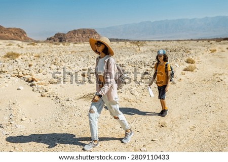 A boy with a backpack and a map walks next to his mother through the desert. Family trekking. Timna National Park. The child is actively spending time. Trekking and hiking.