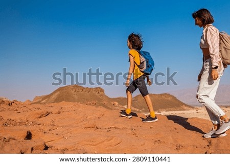 A boy with a backpack and a map walks next to his mother through the desert. Family trekking. Timna National Park. The child is actively spending time. Trekking and hiking.
