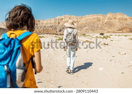 A boy with a backpack and a map walks next to his mother through the desert. Family trekking. Timna National Park. The child is actively spending time. Trekking and hiking.