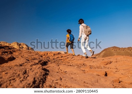 A boy with a backpack and a map walks next to his mother through the desert. Family trekking. Timna National Park. The child is actively spending time. Trekking and hiking.