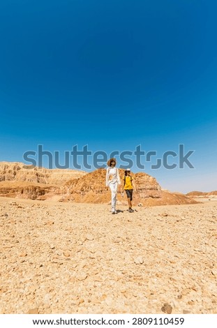 A boy with a backpack and a map walks next to his mother through the desert. Family trekking. Timna National Park. The child is actively spending time. Trekking and hiking.