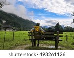 boy with backpack sitting on bench in the middle of mountains bavarian Germany Alps in front of beautiful green field view fog on horizon