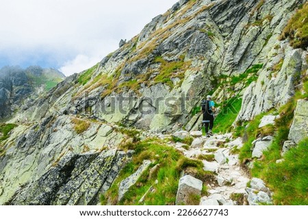 Boy with backpack are walking on a stone path in mountains. Hiker on a trip in the mountain. Tourist on rocky steep mountain slope.