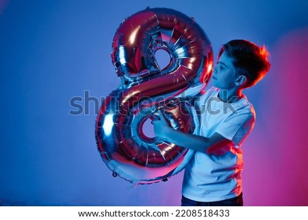 A boy with a balloon in the form of an eight in neon light.
