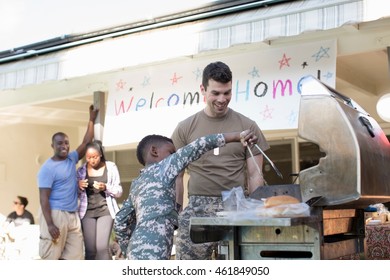 Boy Barbecuing Burgers With Male Soldier At Homecoming Party