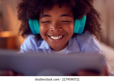 Boy In Bedroom Lying On Bed Wearing Headphones Using Digital Tablet - Powered by Shutterstock