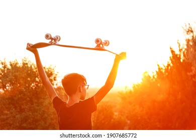 boy from behind with his skateboard during sunset