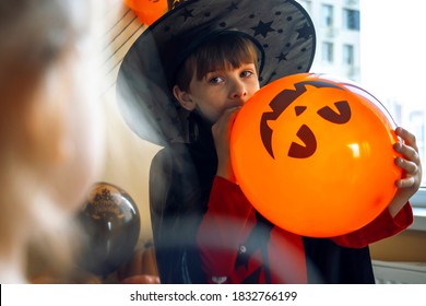 Boy in a black cape and a witch's hat blows a balloon with the image of a pumpkin jack. The child decorates the house for Halloween. - Powered by Shutterstock