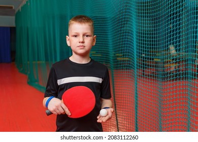 A Boy In A Black T-shirt Holds A Racket And A Table Tennis Ball Indoors