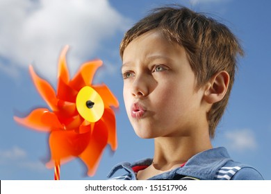 A Boy Blowing A Bright Orange Fan. 