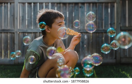 Boy blowing bubbles while crouching at backyard Stock Photo