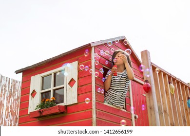 Boy Blowing Bubbles From A Wooden Playhouse