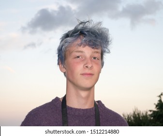 The Boy With Blue Hair. Colour Image Of The Head And Shoulders Of A Teenage Boy With Faded Dyed Blue Hair, Against An Early Evening Sky With Faint Grey Clouds