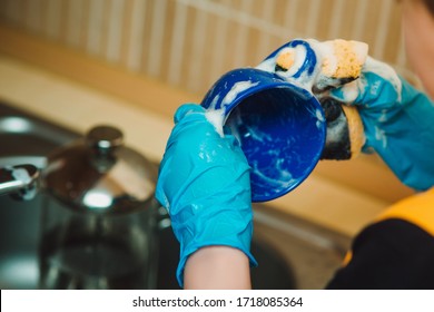 The Boy In A Blue Rubber Glove Holds A Sponge In His Hands. The Boy Helps His Mother In The Kitchen With Cleaning Dirty Dishes. Mom's Assistant.