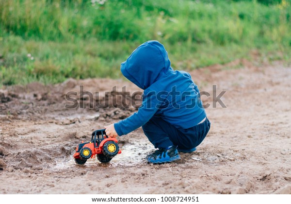 the boy in the blue suit covered in mud plays with a\
toy car in the dirt