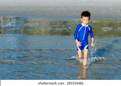 Boy In Blue Swim Suit Run In On The Beach And Sea