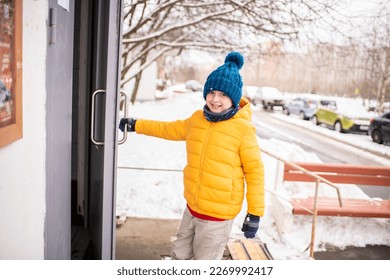 a boy in bright clothes opens the door to the entrance in winter, the child returns from school in cold weather alone - Powered by Shutterstock