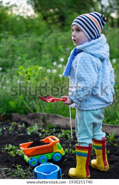 Boy in bright clothes plays on black soil in the\
garden with a toy dump\
truck