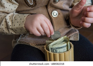 A Boy In A Brown Suit Piles Money In A Piggy Bank. Coins And Banknotes In A Hand. Money Saving Concept. Extra Storage Space For Cash. Stock For A Rainy Day. Financial Literacy