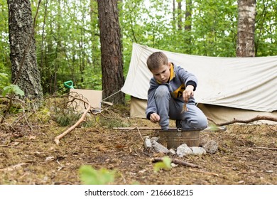 A Boy Building A Fire In A Fire Pit Made Out Of Bucket Near The Tent In The Forest. Starting A Campfire- Starting A Fire Using A Fire Striker- Bushcraft And Primitive Skills.