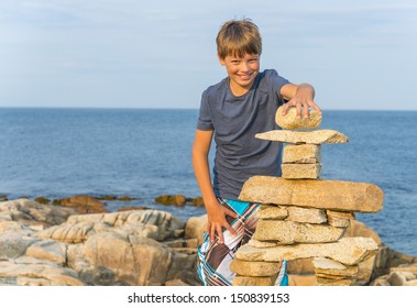 Boy Building Inukshuk On The Rocky Beach (Duncan Cove, Nova Scotia, Canada)