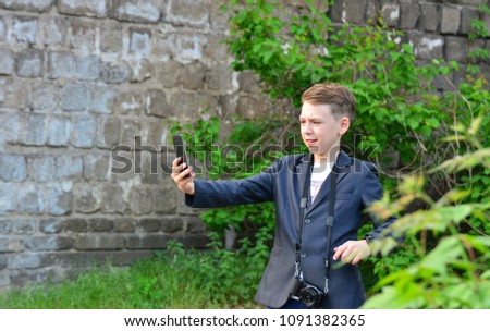 A boy with a camera does selfie on a smartphone, on the street