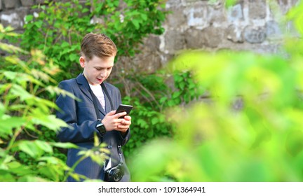 A boy with a camera is writing a message on a smartphone, on the street