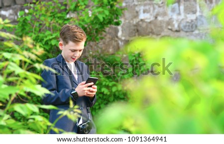A boy with a camera is writing a message on a smartphone, on the street