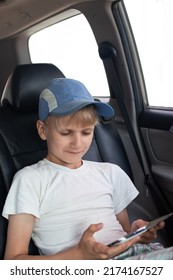 A Boy In A Cap Sits In The Back Seat Of A Car, Looks At The Phone Screen And Smiles.