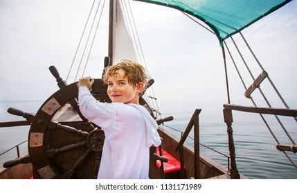 Boy as a captain or sailors play on the ship outdoors on sunny day. Kid driving boat. Captain at the helm controls of a sailing boat in sea.