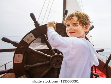 Boy as a captain or sailors play on the ship outdoors on sunny day. Kid driving boat. Captain at the helm controls of a sailing boat in sea.