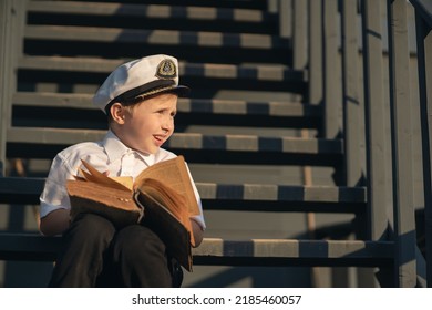 The boy is the captain of the ship. A boy in the form of a ship captain listens to a sea shell. Dream about the sea. Future captain. Model of a ship in the park