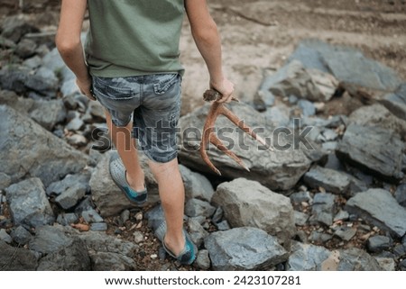 Boy carrying a deer shed antler across rocky landscape