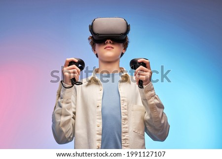 boy in casual outfit using VR glasses exploring augmented reality, using smart devices, controllers in hands. Modern cyber technologies concept, Virtual reality games. isolated on colourful background