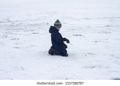 A Boy Catches Fish In Winter With A Fishing Rod On The Ice Of The River On A Winter Fishing Trip.