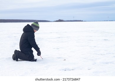 A Boy Catches Fish In Winter With A Fishing Rod On The Ice Of The River On A Winter Fishing Trip.