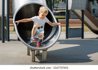 Boy Child Climbing Sliding And Playing On Metal Slide On Outdoor Playground In Summer Park. Activity And Amusement Center In Kindergarten Or School Yard. Toddler Kid Outdoors.