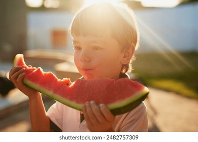 Boy, child and eating watermelon in backyard, summer or outdoor for wellness, nutrition and holiday. Kid, fruit and hungry with diet, mess and memory for vacation with sunshine on lawn at family home - Powered by Shutterstock