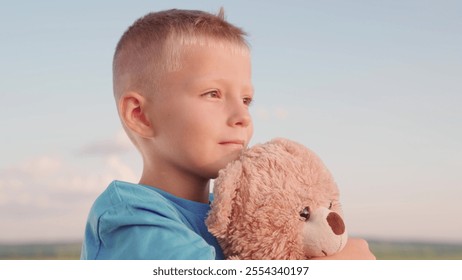 Boy child hugging friend teddy bear. Little boy hug his favorite soft friend on playground. Child play with teddy bear. Plush toy in boy hands, kid in summer park. Thoughtful kid looking into distance - Powered by Shutterstock