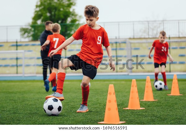 Boy in children\'s soccer team on training. Kids\
practicing outdoor with a soccer balls. Training football session\
for children on soccer camp. Young boy improving dribbling skills.\
Training with cones
