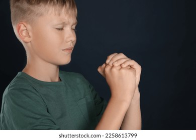 Boy with clasped hands praying on black background, space for text - Shutterstock ID 2258613799