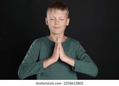 Boy with clasped hands praying on black background - Shutterstock ID 2258613805