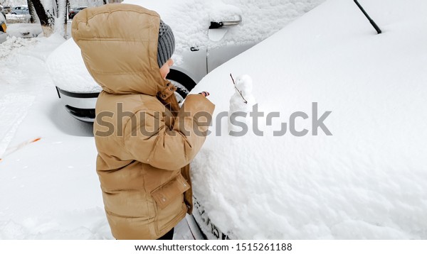 Boy clean up snow covered car after snow fall .\
In the cold winter morning