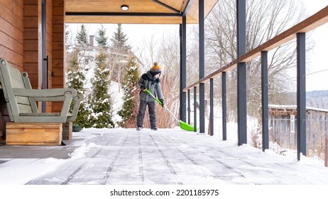 The Boy Cleans The Snow On The Terrace Of His House With A Big Shovel. Family Lifestyle In Winter. The Child Is Doing Household Chores. Kid Shoveling Snow On Sunny Day.